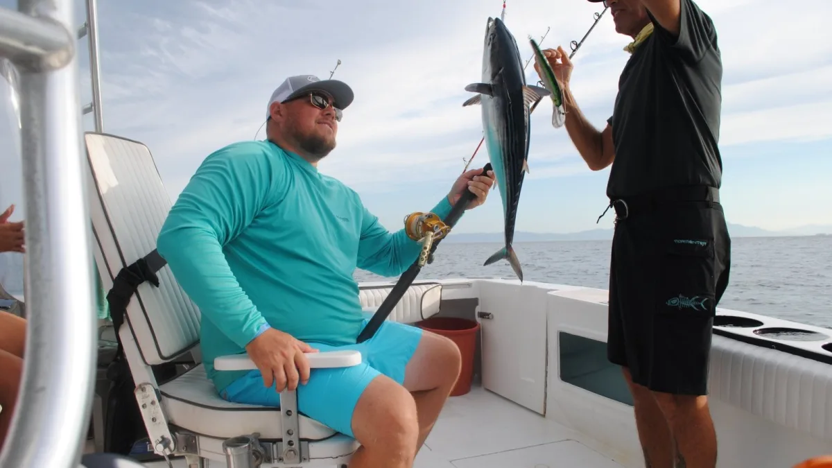 A mate unhooking a bonito for a guest during a fishing charter inside Banderas Bay